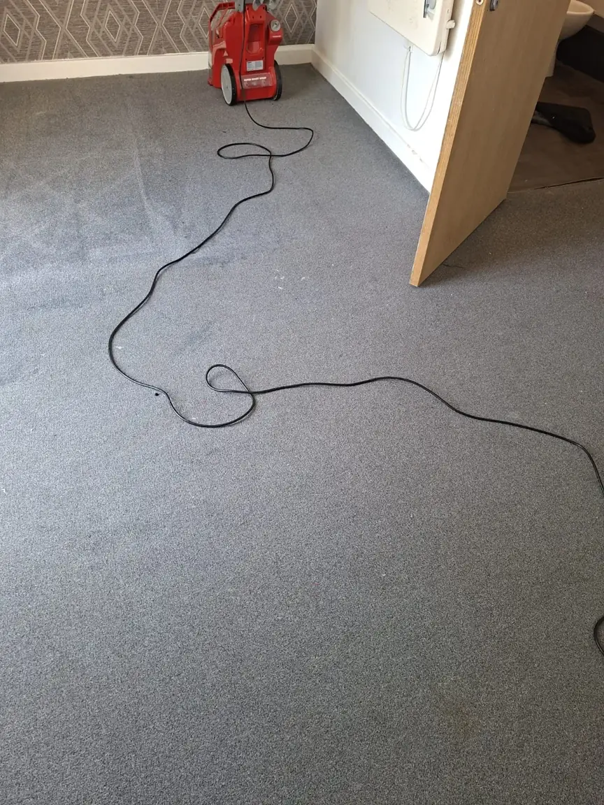 View through an open door of grey carpet, cleaning lines and a red cleaning machine