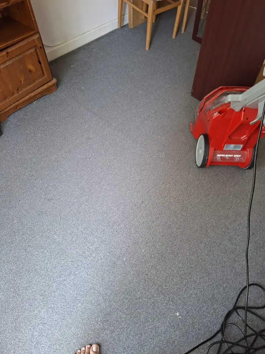 Carpeted floor between wooden furniture with a red carpet-cleaning machine at the edge