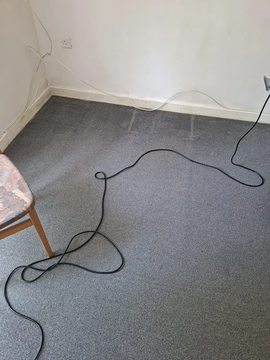 Grey carpet at a white-walled room corner with visible cleaning passes and a machine cable